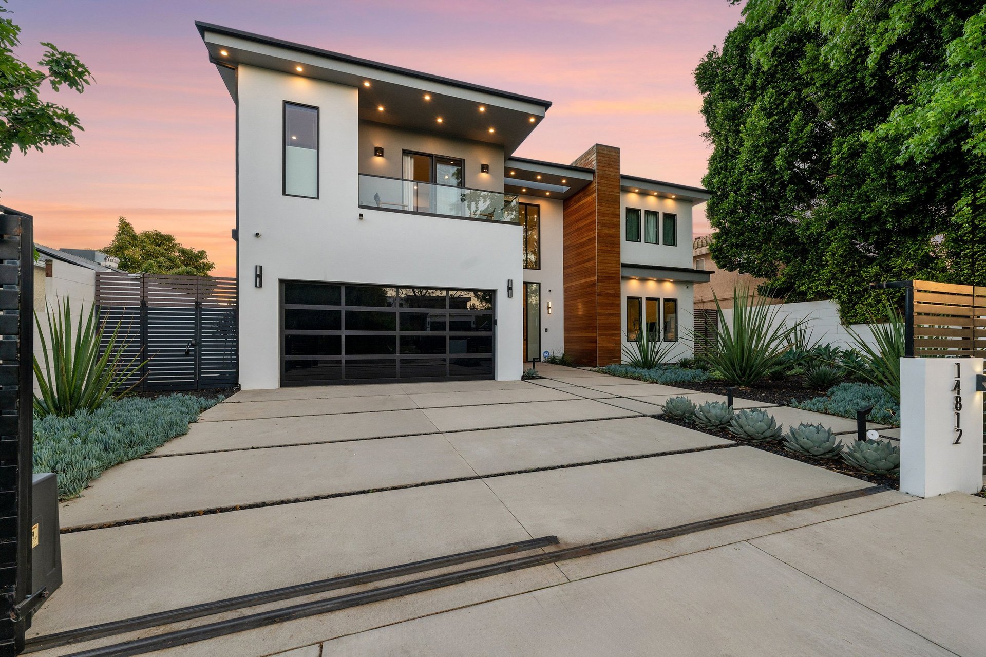 Twilight view of a modern luxury home with garage door, driveway, and pool